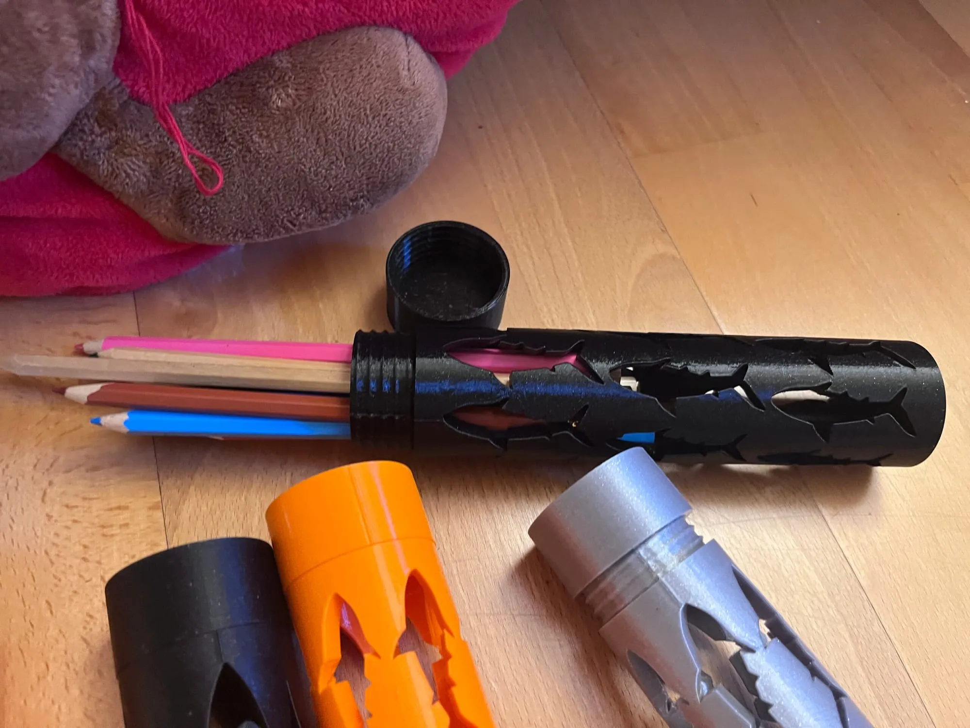 Étui noir ouvert d’où sortent des crayons de couleur, entouré d’étuis orange, noir et argent