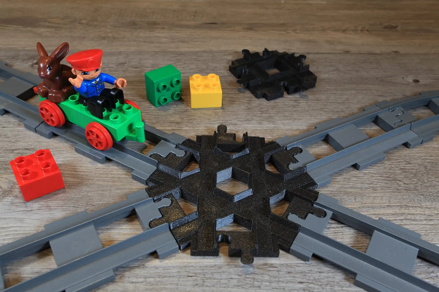 Duplo-Zug mit Lokführer auf der schwarzen, 3D-gedruckten 6-Wege-Kreuzung zwischen Steinen