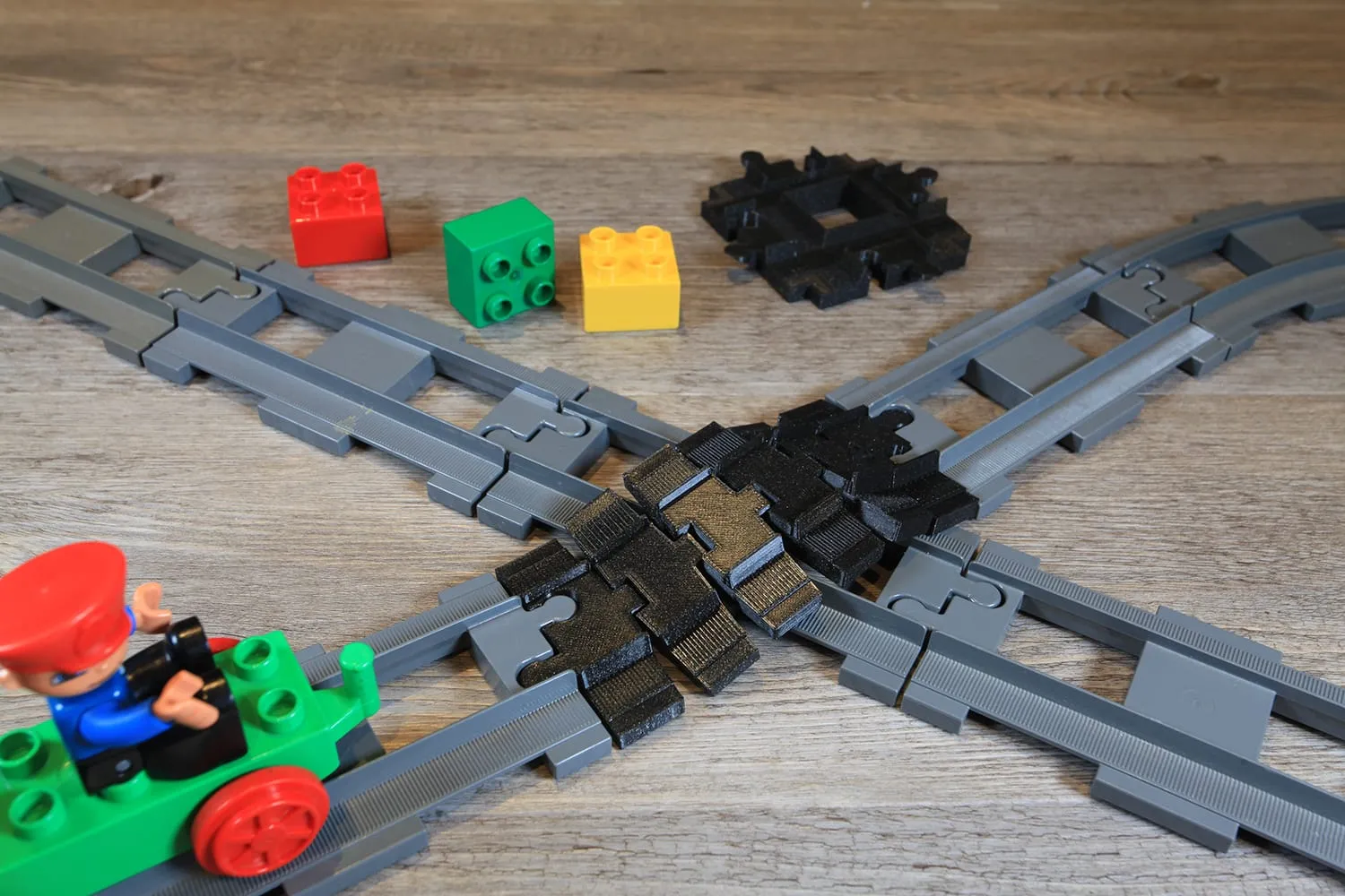 Rail flexible noir au centre d’un croisement de rails DUPLO, un train vert approche