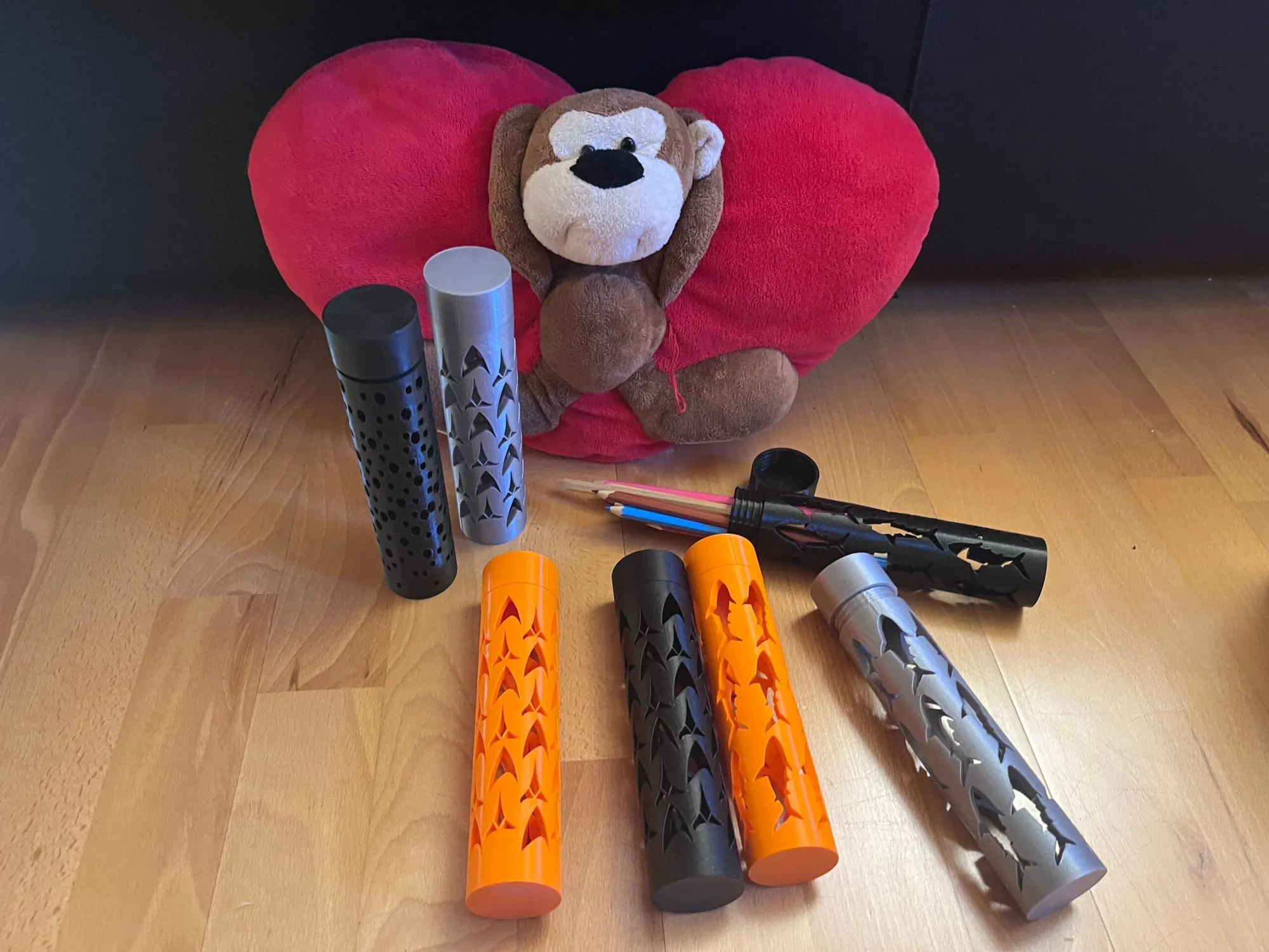 Série d’étuis cylindriques noirs, argent et orange alignés devant une peluche singe