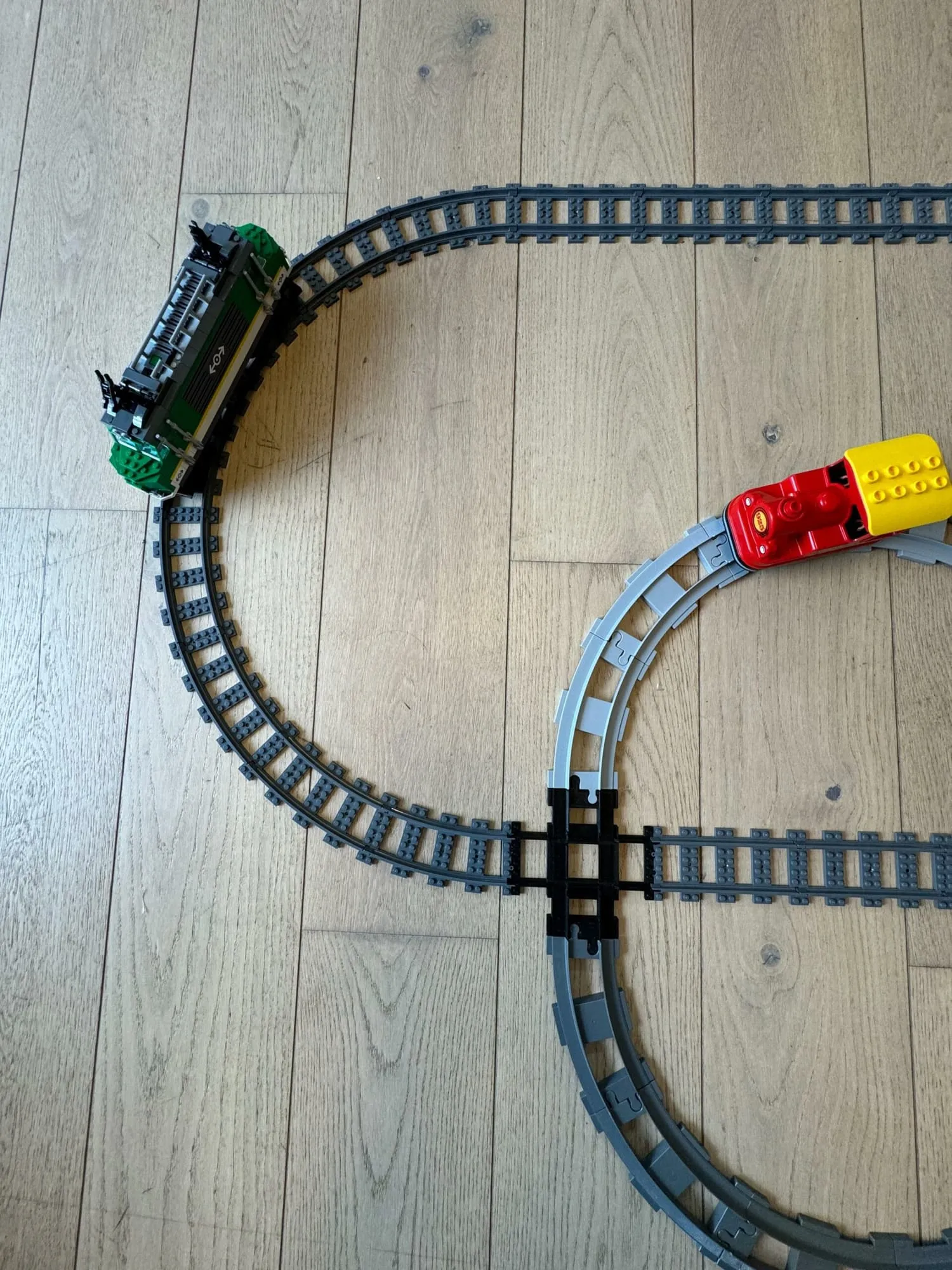 Circuit de train avec le croisement noir : une locomotive verte à gauche et un train DUPLO rouge et jaune à droite