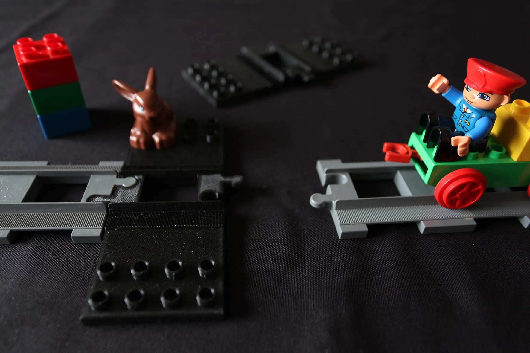 Plaque noire posée entre les rails DUPLO, avec un lapin, une tour de briques et un train qui arrive