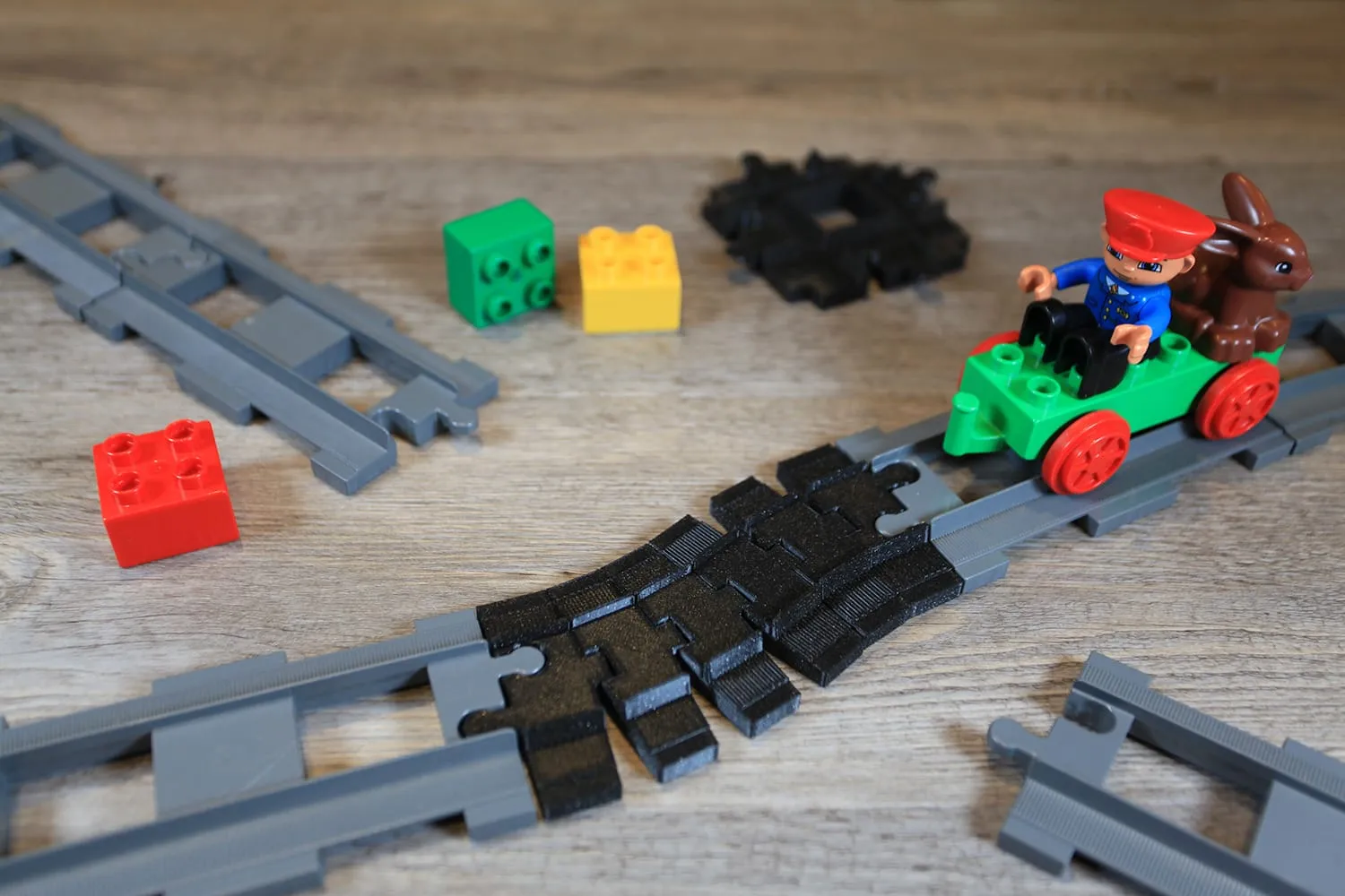 Train DUPLO vert et son conducteur roulant sur un rail flexible noir entre des rails gris